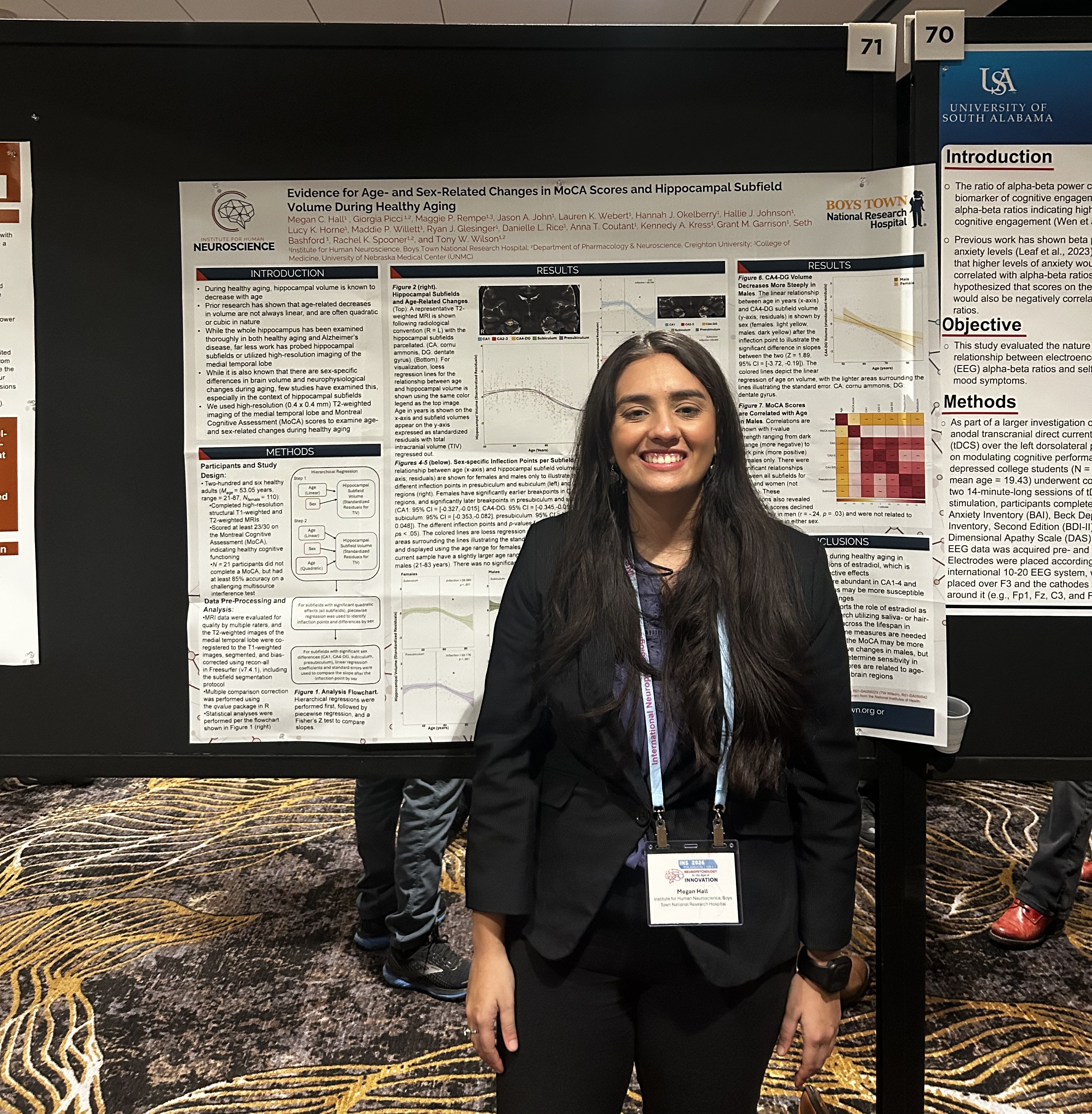 a woman with brown skin and dark hair is wearing professional clothing and standing next to a scientific poster