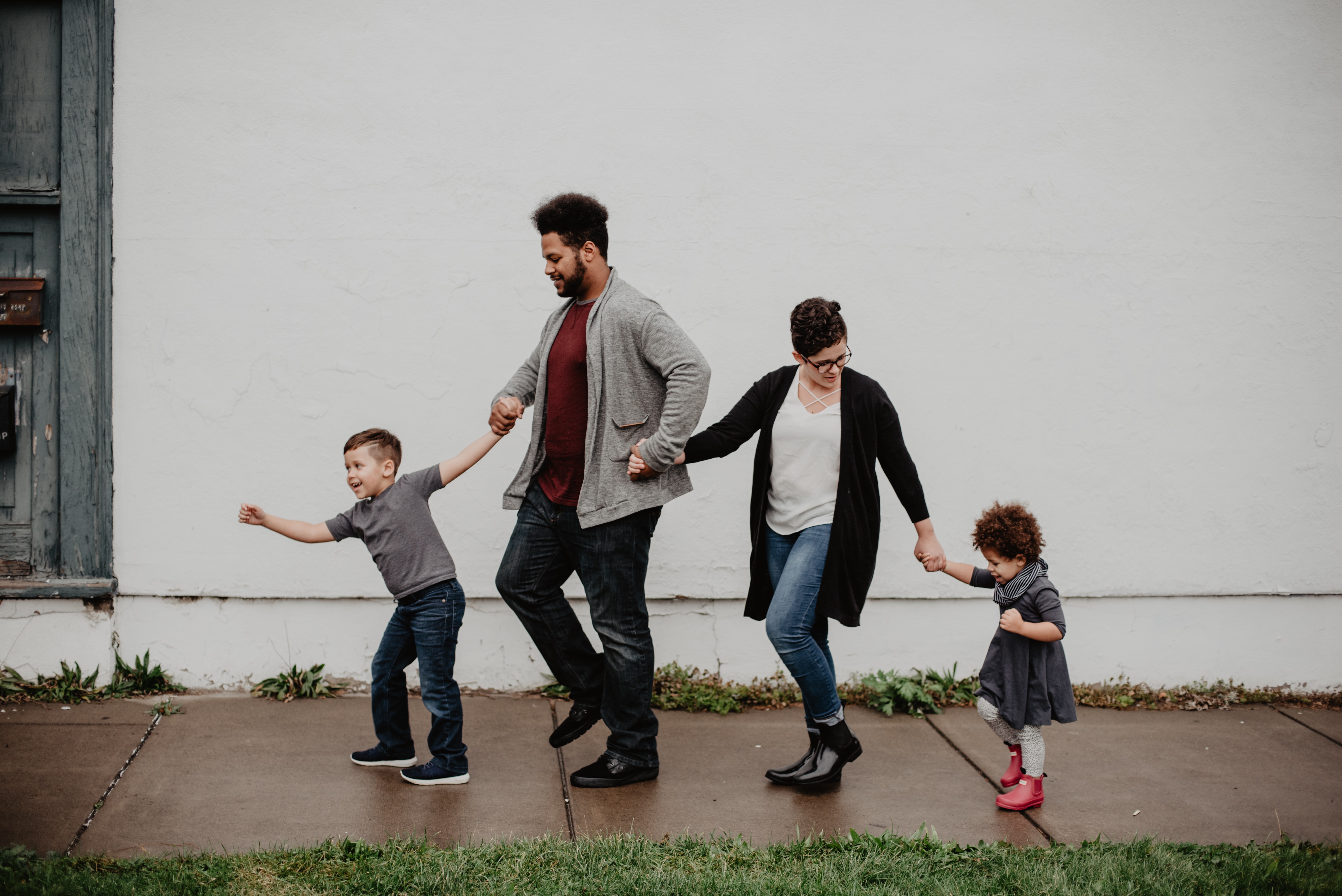 two adults and two toddlers walk along the sidewalk holding hands